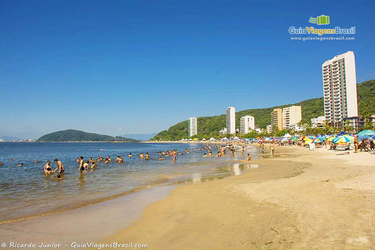 Imagem de turistas nas águas calmas e alguns prédios que possui na orla da Praia Mansa, em Caiobá, Santa Catarina, Brasil.