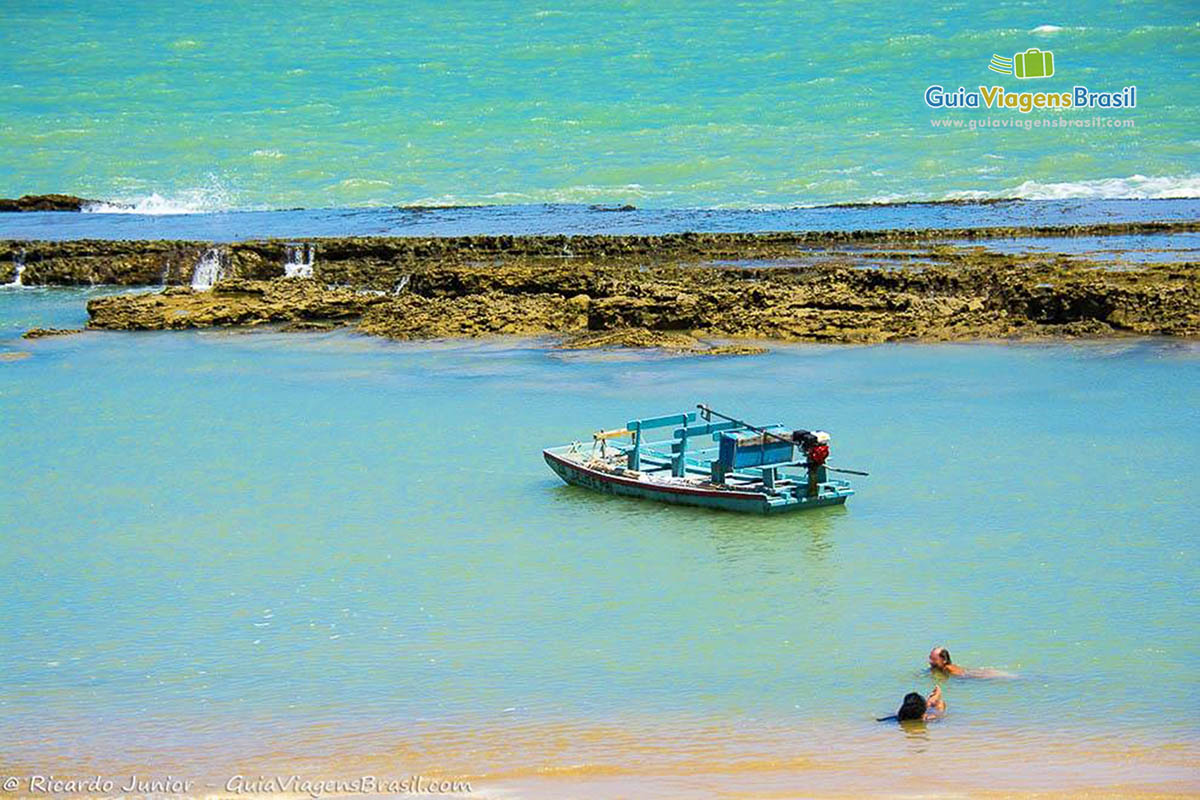 Imagem de barco parado e dois turista se banhando na piscina natural de Pontal do Coruripe, em Alagoas, Brasil.