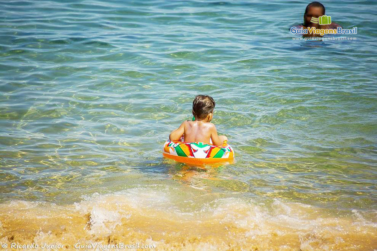 Imagem de criança com bóia nas águas quentes da praia.
