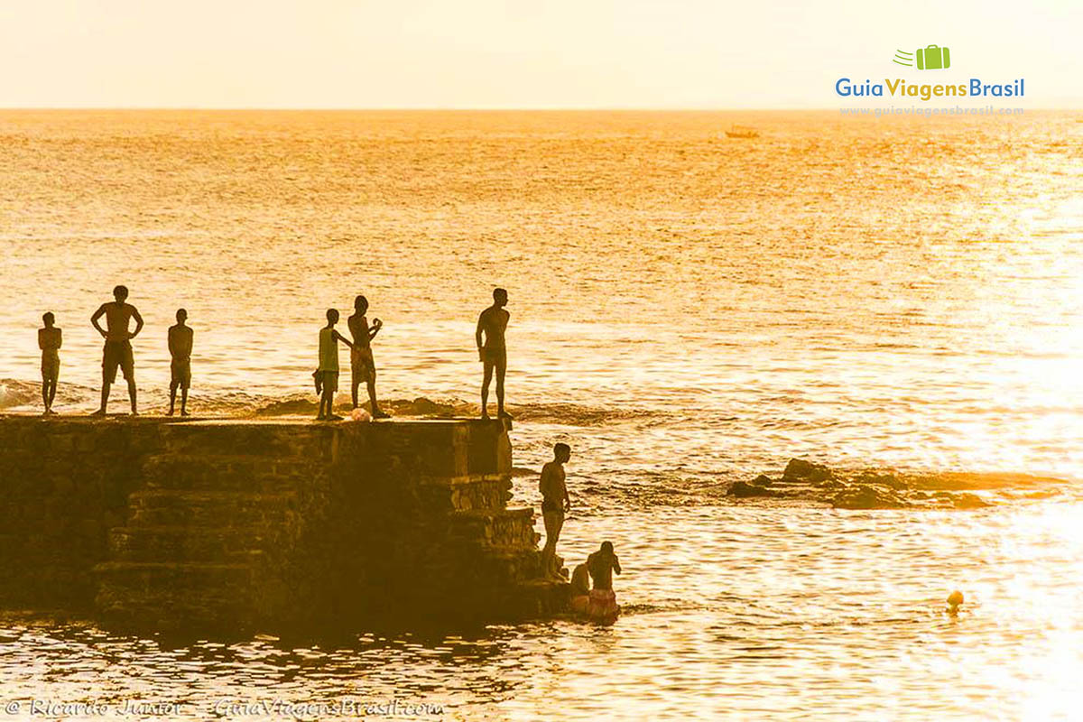 Imagem de turistas pulando no mar com uma luz do sol maravilhosa.