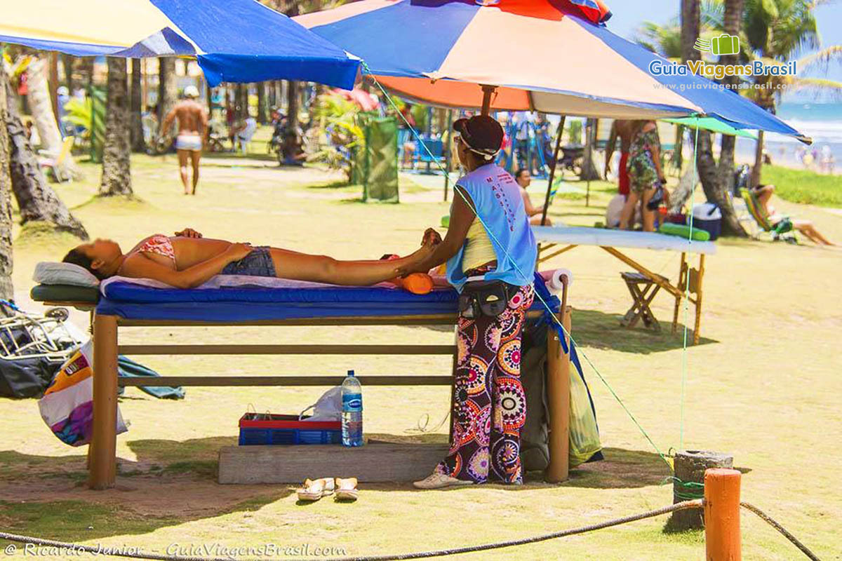 Imagem de turista recebendo massagem em uma maca na praia.