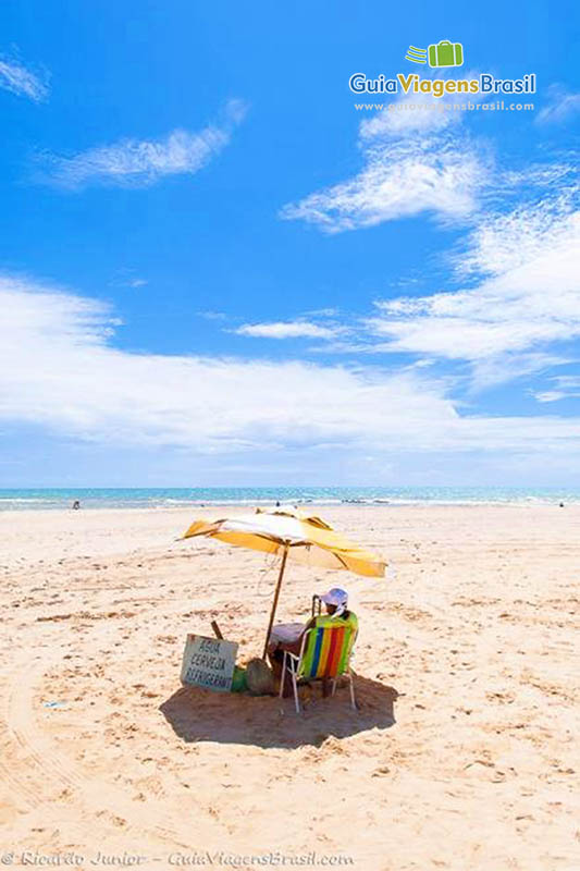 Imagem de uma turista sentada em sua cadeira e embaixo de guarda sol amarelo na Praia Canoa Quebrada.