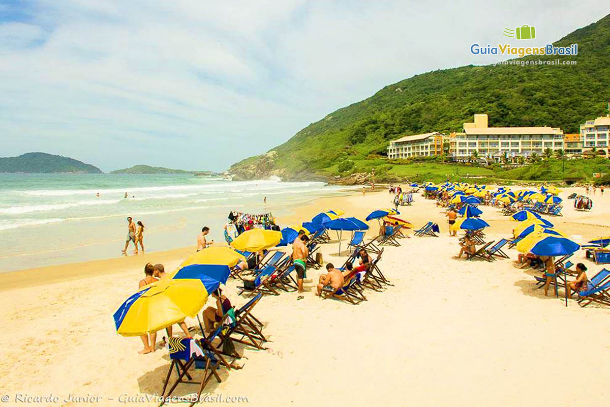Imagem de vários guarda sol coloridos na praia e turistas.