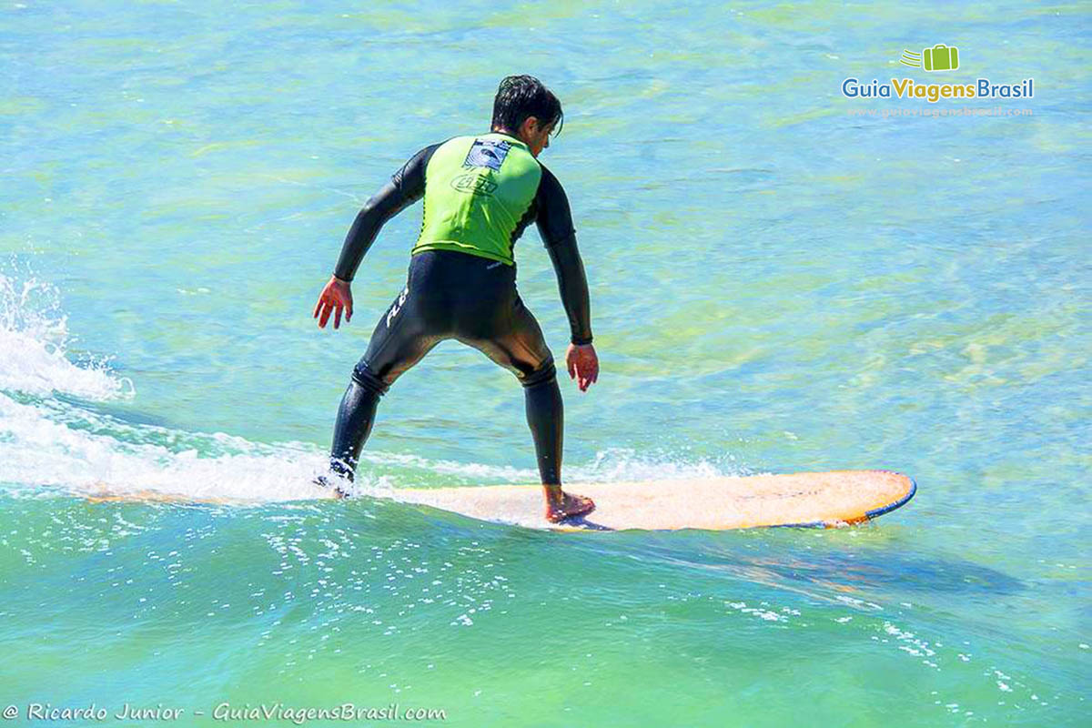 Imagem de surfista em cima da prancha nas águas translúcidas da Praia Joaquina.