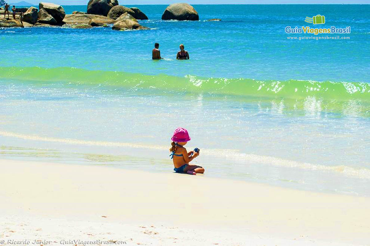 Imagem de uma menina na beira da praia brincando.