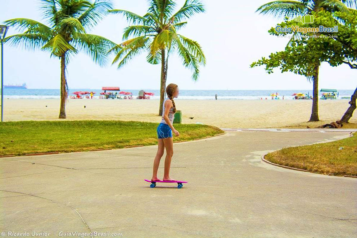 Imagem de menina andando de skate no calçadão na praia.