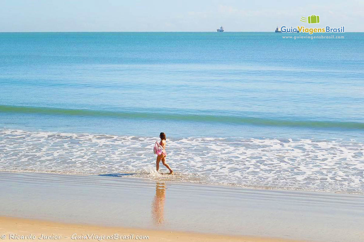 Imagem de uma moça caminhando com o pés na água do mar.