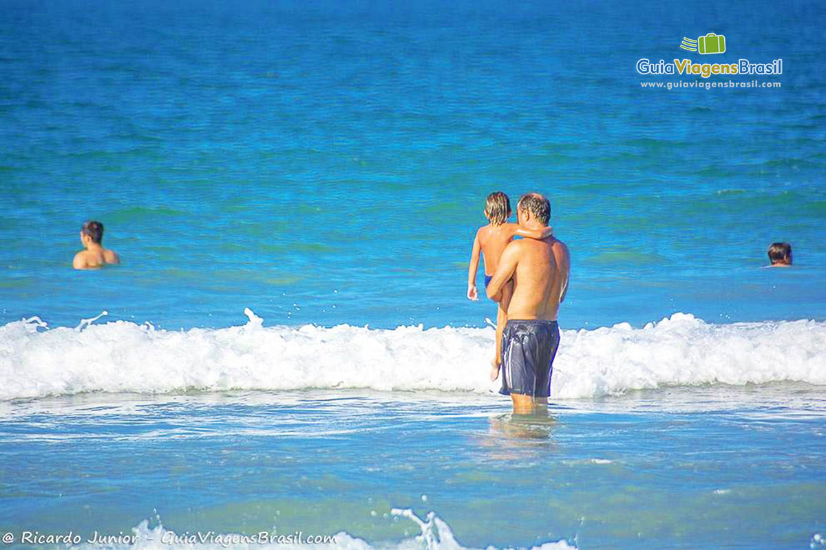 Imagem de pai entrando com filho no colo nas águas da Praia Bombas.