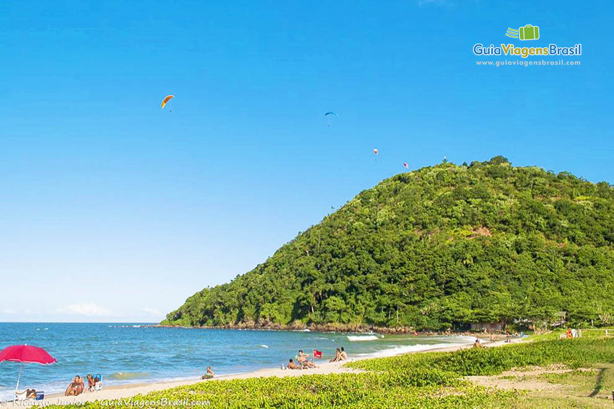 Imagem de pessoas voando de paraglider na bela Praia dos Amores.