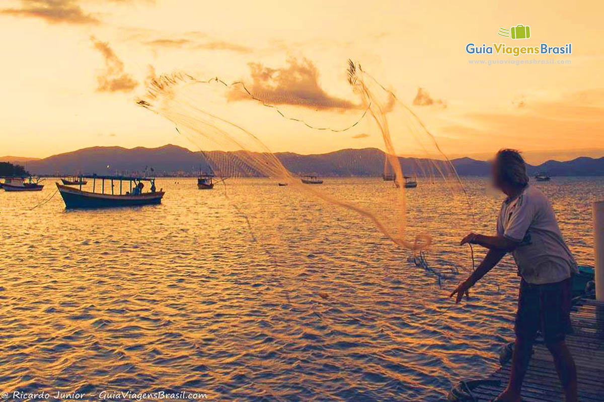 Imagem de um pescador jogando a rede no mar.