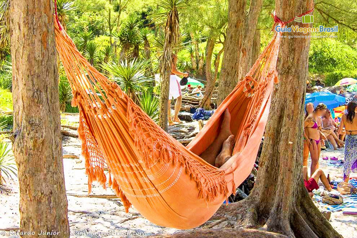 Imagem de uma rede pendurada em árvores  e uma pessoa deitada descansando.