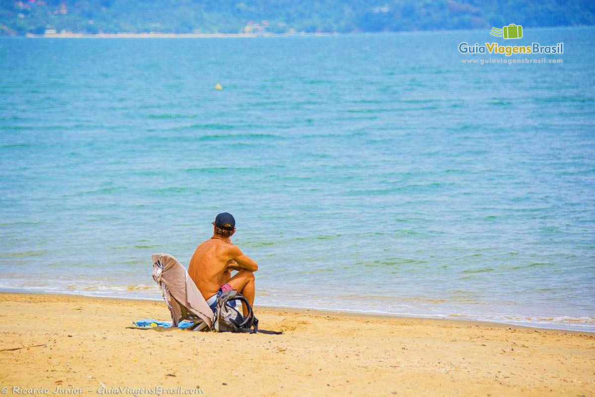 Imagem de rapaz sentado admirando o mar.