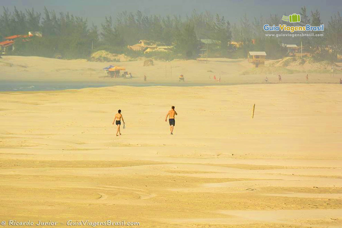 Imagem de duas pessoas caminando nas areia da praia.