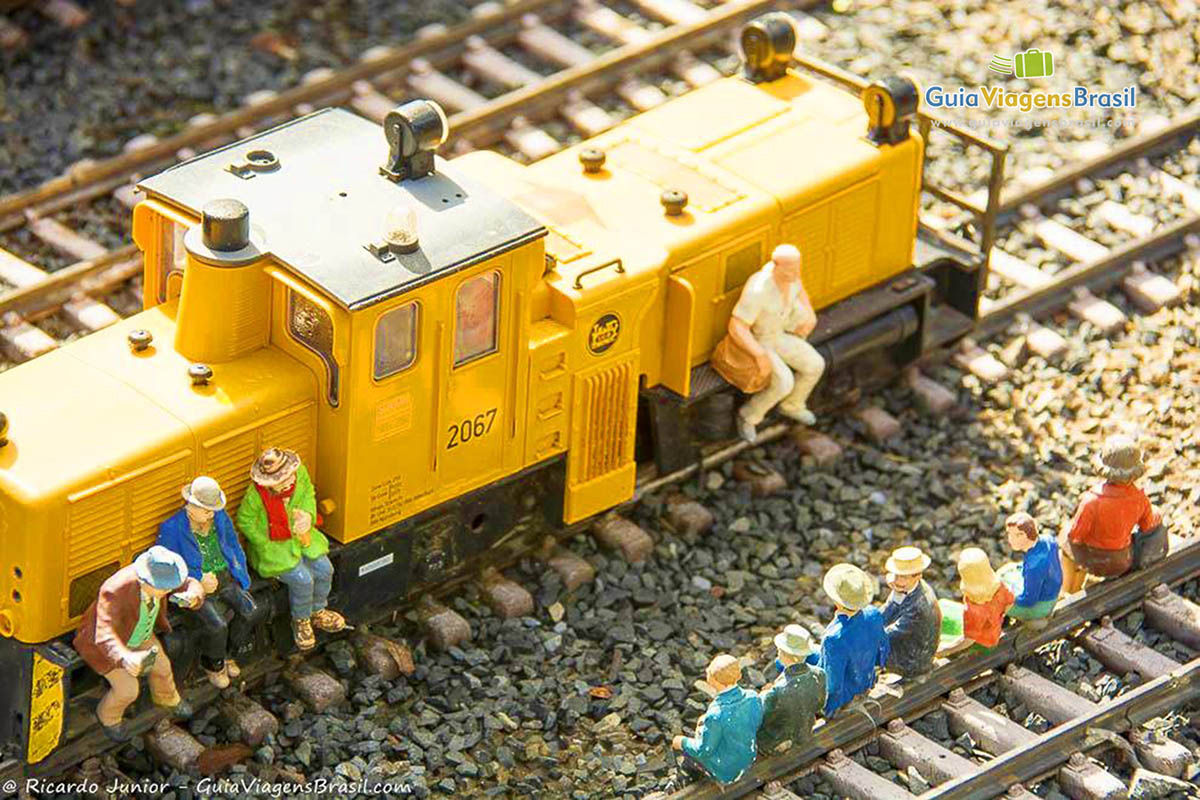 Imagem de miniaturas de pessoas sentadas no trem e nos trilhos.