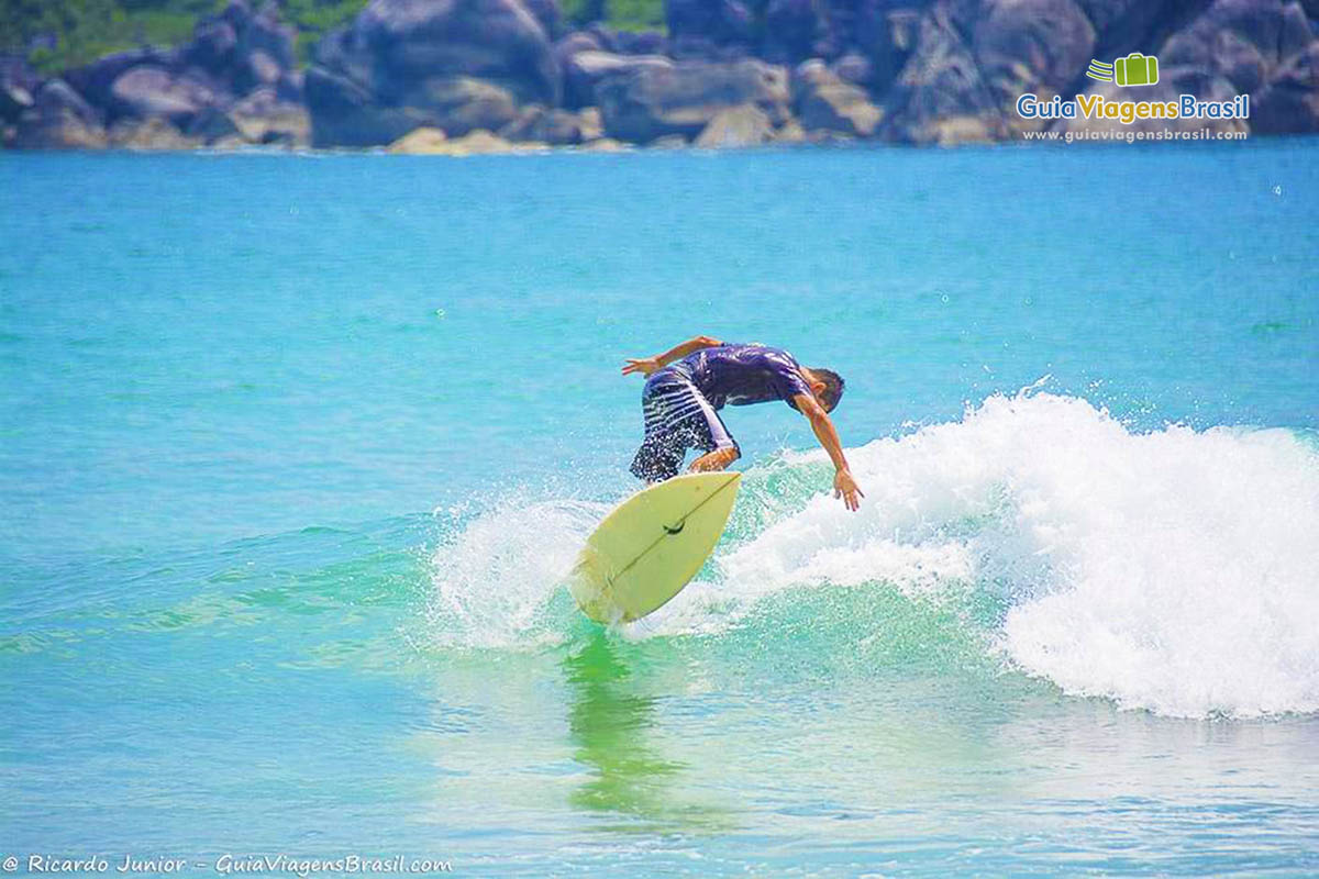 Imagem de um menino surfando na bela praia.
