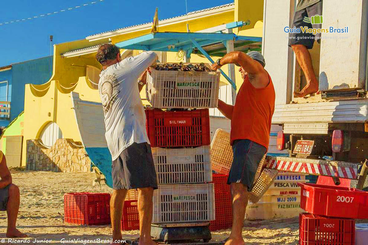 Imagem de pescadores com seus pescados em caixas.