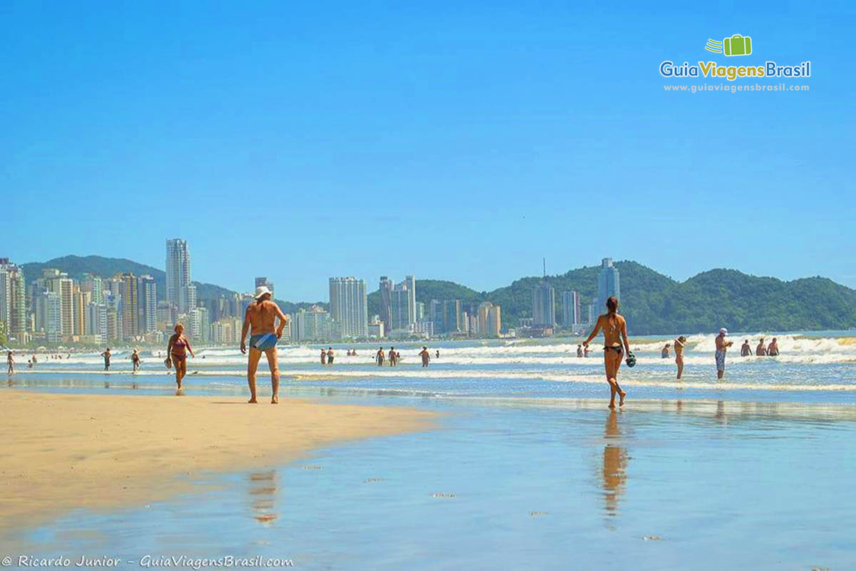 Imagem de pessoas andando na beira da praia em um lindo dia.