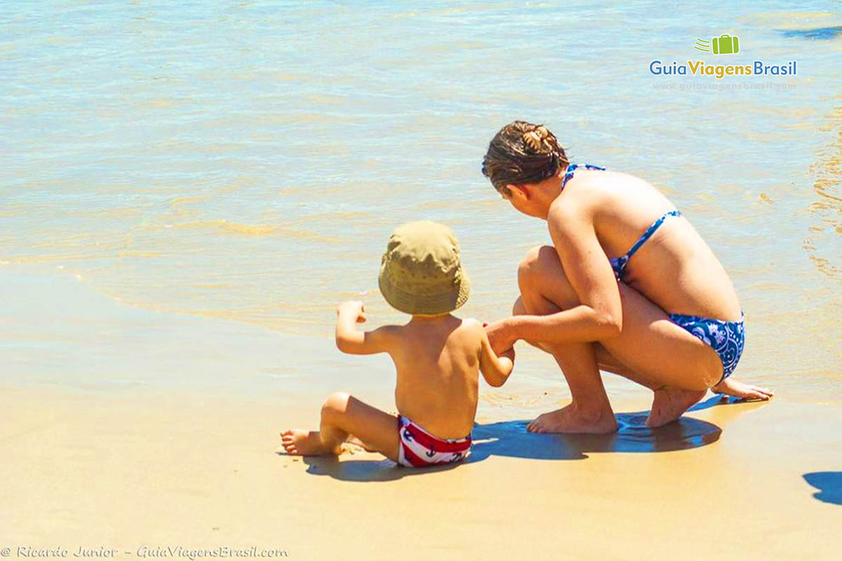 Imagem de mãe e filho brincando na beira da praia.