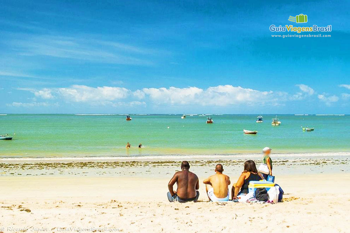 Imagem de três amigos sentados nas areias da Praia Pajuçara.