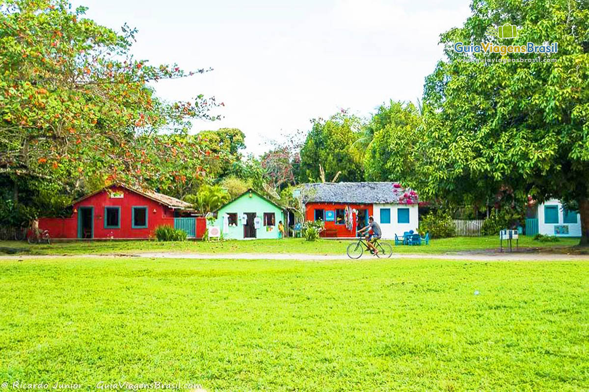Imagem de um morador andando de bicicleta no meio do gramado e ao fundo as lindas casas coloridas.