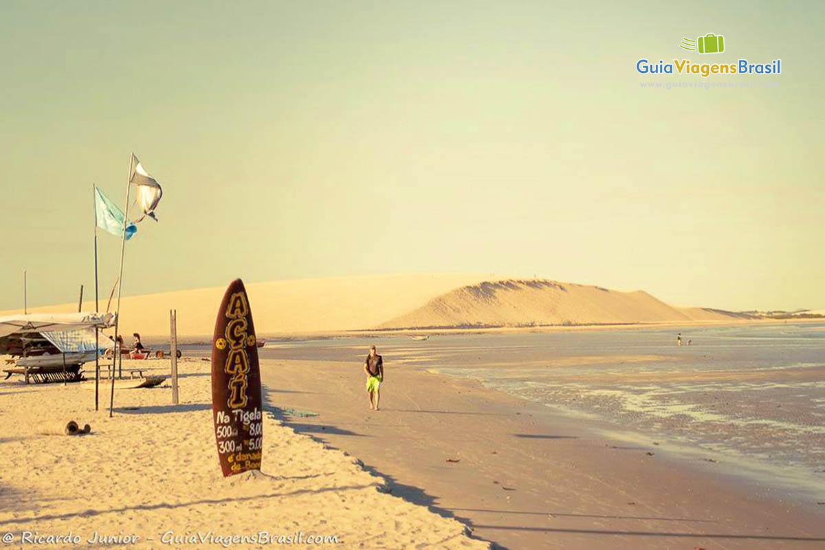 Imagem de fim de tarde e um anúncio de venda de açaí em uma prancha na areias da praia.