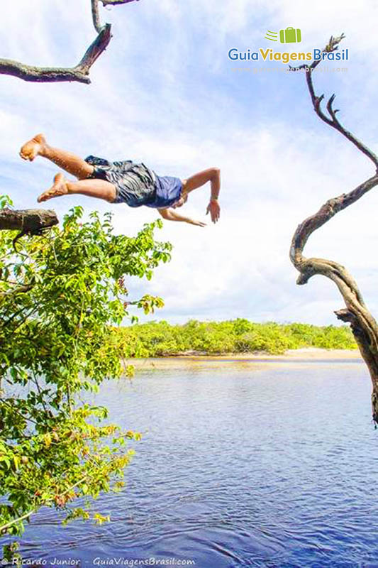 Imagem de um rapaz pulando de uma madeira nas águas da lagoa.