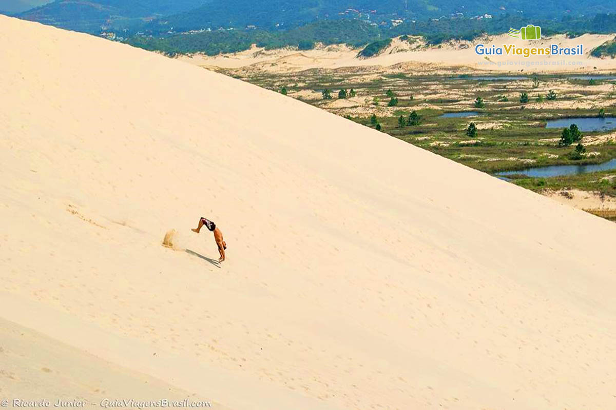 Imagem de um rapaz saltando nas dunas.