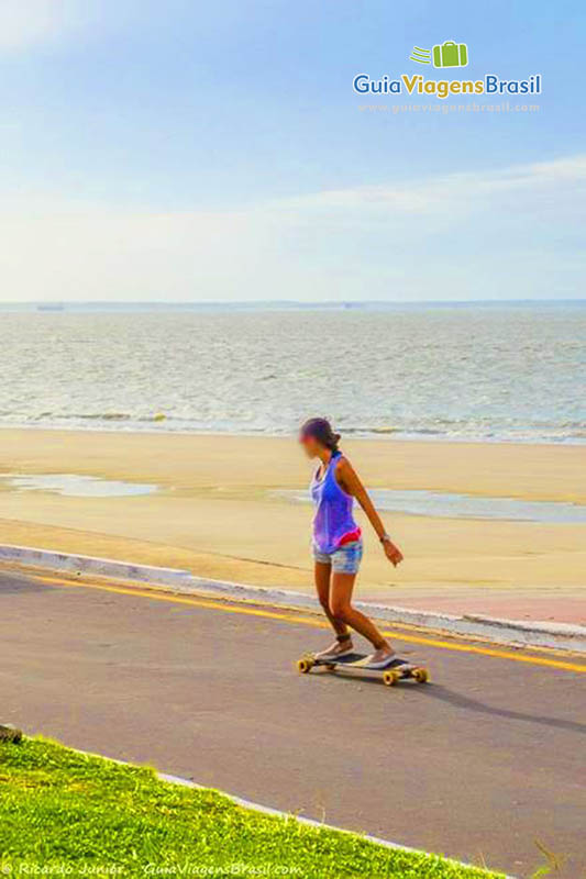 Imagem de uma menina andando de skate no calçadão da praia.