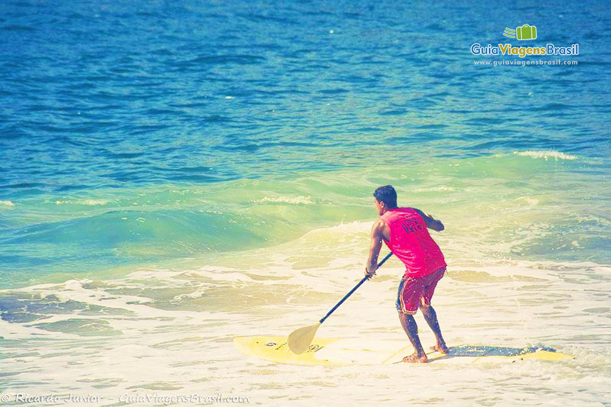 Imagem aproximada de uma pessoa praticando stand up paddle nas águas da praia.