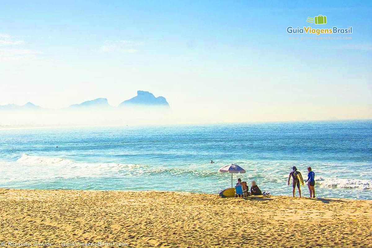 Imagem de surfistas reunidos na areia da Praia Recreio dos Bandeirantes.