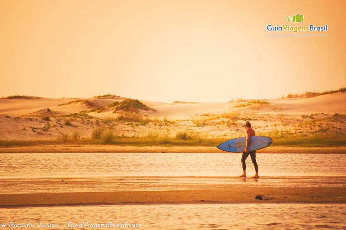 Imagem de um surfista andando na areia da praia em um belo entardecer na Praia Guarda do Embaú.