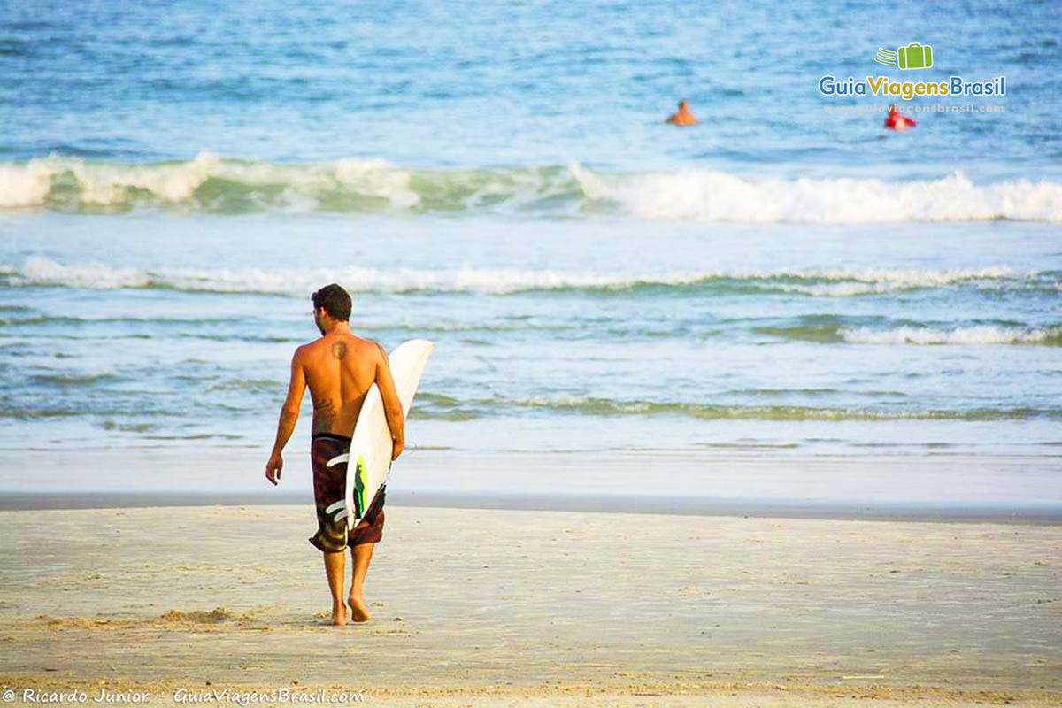 Imagem de sufista andando com sua prancha nas areias da Praia das Pitangueiras.