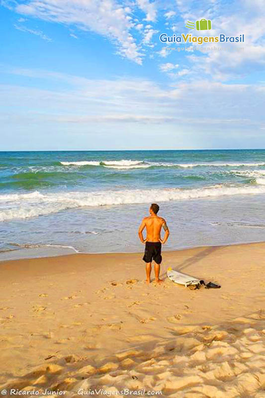 Imagem de surfista com prancha na areia olhando as ondas da Praia do Futuro.