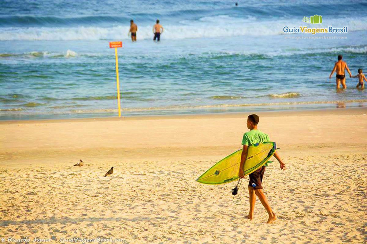 Imagem de surfista andando com sua prancha pelas areias da Praia do Tombo.