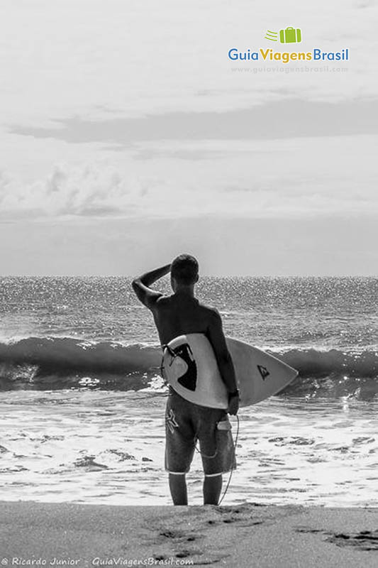 Imagem preto e branco e um surfista de costas olhando para o mar.