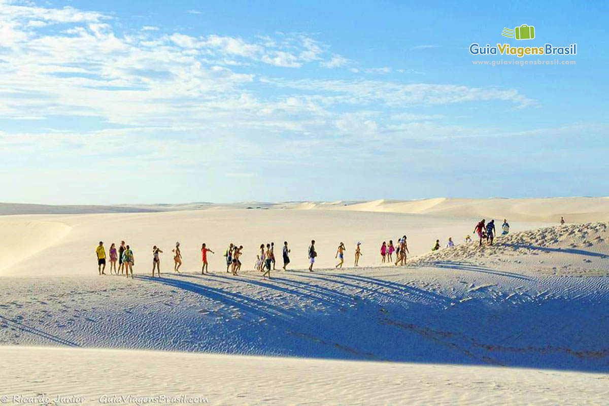 Imagem de turistas andando sobre as dunas próximo as águas cristalinas da Lagoa Azul.