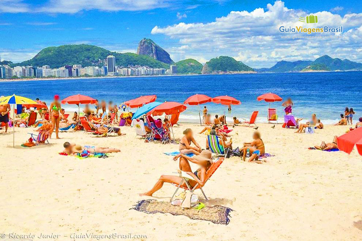 Imagem de turistas nas areias da praia, curtindo o lindo dia de sol.